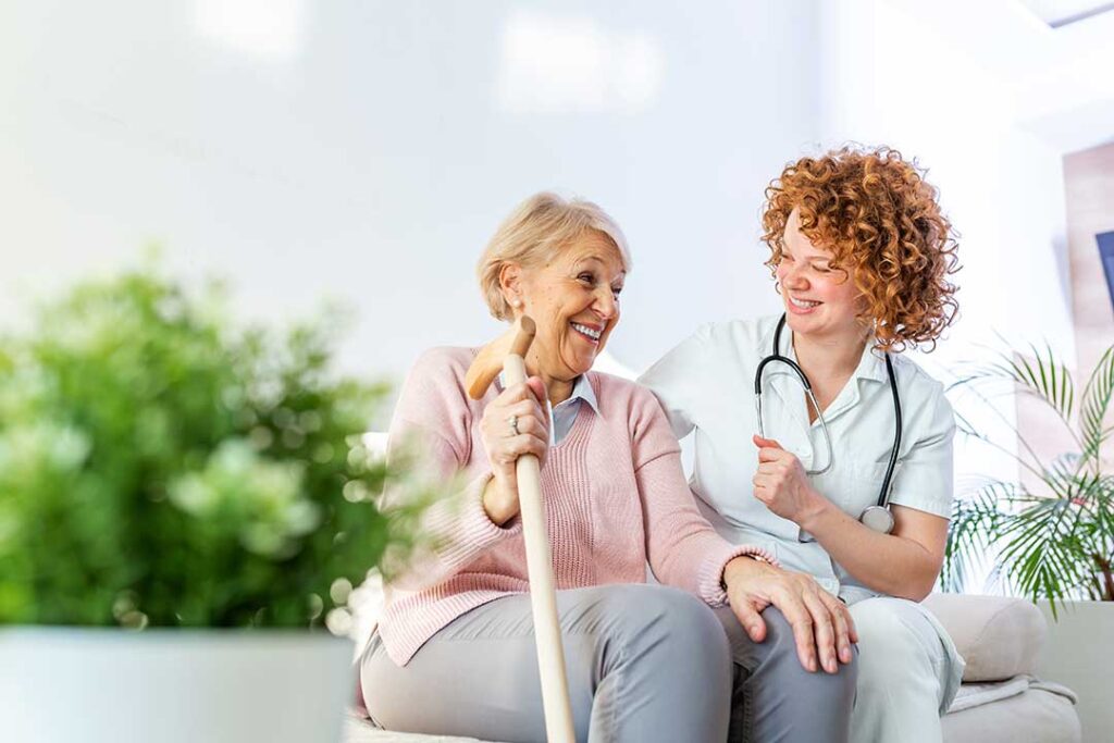 Older adults share a meal in a bright assisted living dining room beside an accessible hallway.