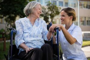 Caregiver helps an older resident walk through a bright assisted living hallway.